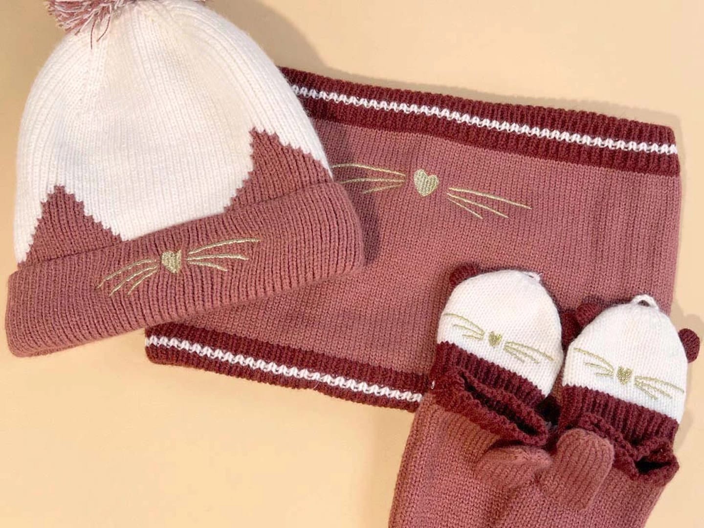 A cozy knit set consisting of a hat, scarf, and mittens adorned with cute cat features, representing Vertbaudet products